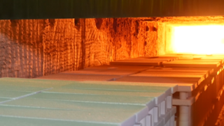 Der Rohling wird bei über 1.700°Celsius in den Sinterofen geschoben aus dem glühende Flammen und Hitze zu sehen sind
